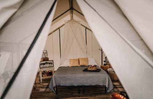 Cozy glamping tent interior featuring a bed, decorative pillows, and rustic decor.