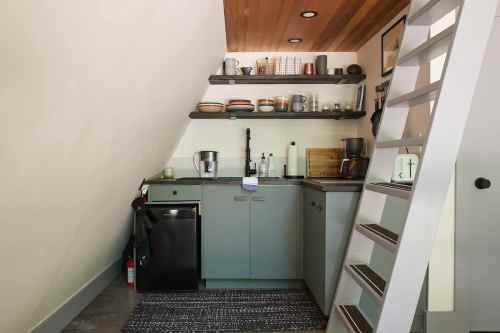 Cozy kitchen with sloped ceiling, shelves of dishes, and a staircase leading to an upper level.