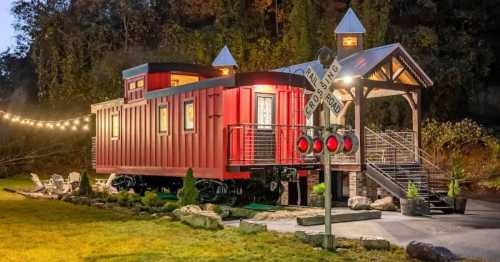 A red train caboose converted into a cozy accommodation, set near a crossing sign and surrounded by greenery.