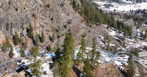 Aerial view of a snowy landscape with a winding roller coaster track and pine trees near a mountain.