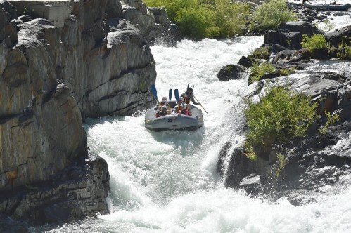 A group of people in a raft navigating through a rocky river with whitewater rapids.