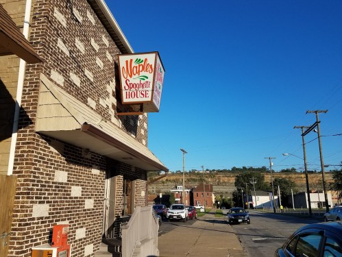 Sign for Naples Spaghetti House on a brick building, with a clear blue sky and a hilly landscape in the background.