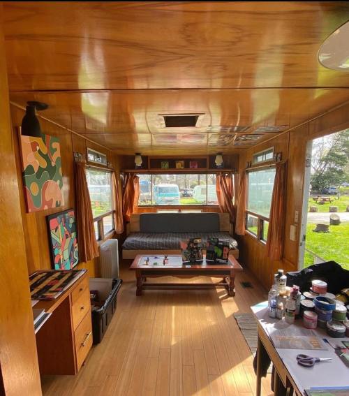 Cozy wooden interior of a cabin with a sofa, coffee table, and art on the walls, surrounded by large windows.