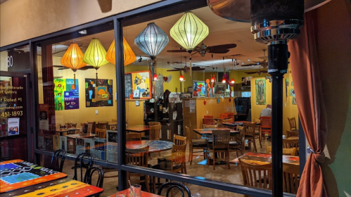 A cozy restaurant interior with colorful lanterns, wooden tables, and vibrant artwork on the walls.