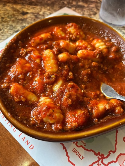 A bowl of gnocchi in a rich meat sauce, garnished and served with a spoon.