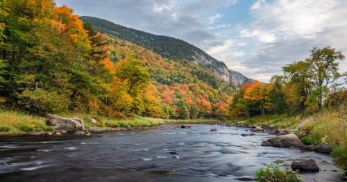 calm waters of the ausable river on a cloudy day and autumn trees nearby