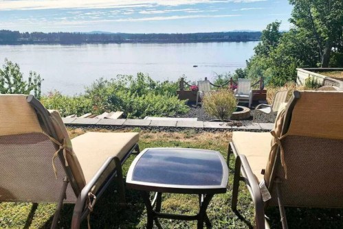 Two lounge chairs facing a serene lake view, with greenery and a small table in between.