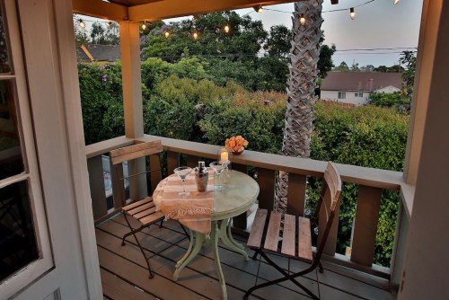 Cozy balcony with a small table, two chairs, and string lights, surrounded by greenery and a candlelit centerpiece.