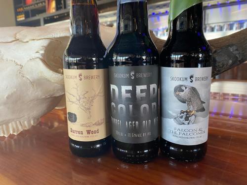 Three bottles of Skookum Brewery beer: Barren Wood, Deep Color, and Falcon & The Falconer, displayed with a skull.
