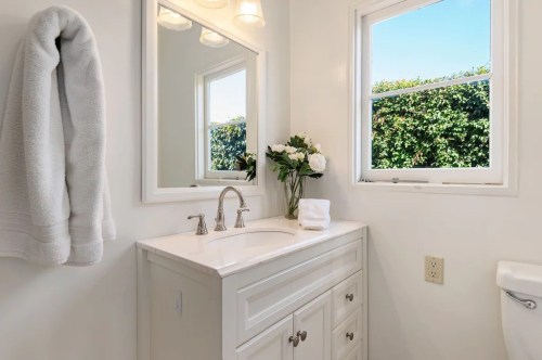 Bright bathroom with a white vanity, mirror, towel, and a window overlooking greenery. Fresh flowers on the counter.