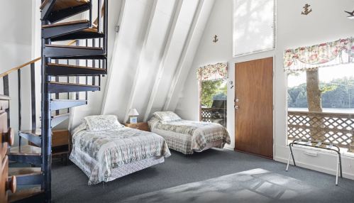 Cozy bedroom with two twin beds, spiral staircase, and large windows overlooking a wooded area.