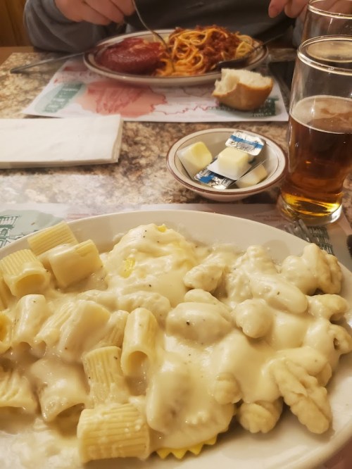 A plate of creamy pasta with rigatoni and gnocchi, accompanied by a glass of beer and a plate of spaghetti in the background.