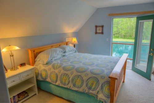 Cozy bedroom with a wooden bed, colorful bedding, and a door leading to a scenic outdoor view.