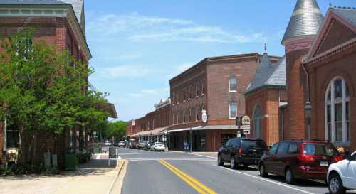 A charming street lined with brick buildings, shops, and parked cars under a clear blue sky.