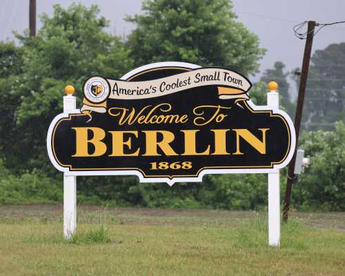 Welcome sign for Berlin, labeled "America's Coolest Small Town," established in 1868, surrounded by greenery.