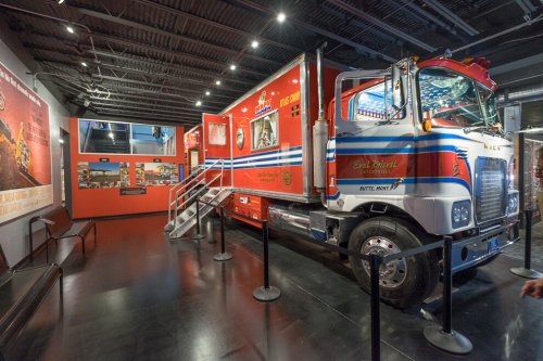 A red fire truck displayed indoors, featuring various graphics and surrounded by barriers in a museum setting.