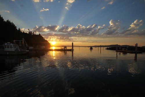 Sunset over a calm harbor, with rays of light breaking through clouds and reflecting on the water.