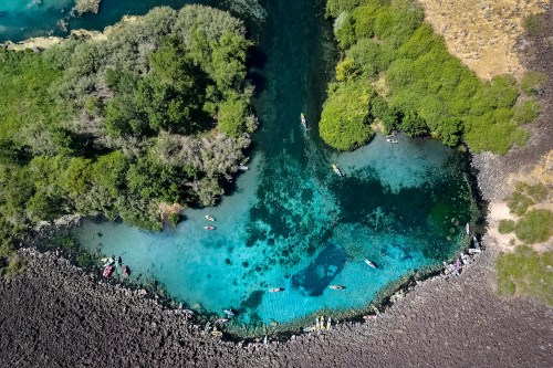 Aerial view of a vibrant blue river surrounded by lush greenery and rocky shores, with kayakers enjoying the water.