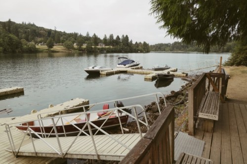 A serene lakeside view with boats docked, surrounded by trees and a wooden walkway.