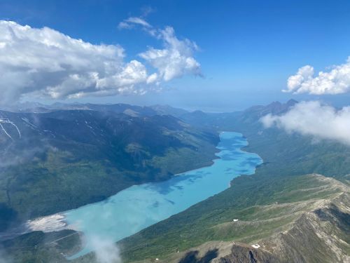 Aerial view of a turquoise river winding through lush green mountains under a blue sky with scattered clouds.