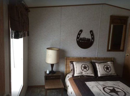 Cozy bedroom with a bed featuring a star-patterned quilt, a lamp, and rustic decor on the walls.