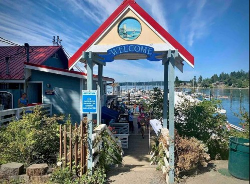 A welcoming entrance to a marina with boats, greenery, and a clear blue sky in the background.