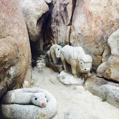 Two stone animal sculptures, one resembling a lion and the other a snake, nestled among large rocky formations.