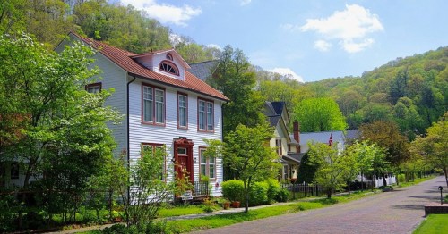 A charming street lined with colorful houses and lush green trees, set against a backdrop of rolling hills.