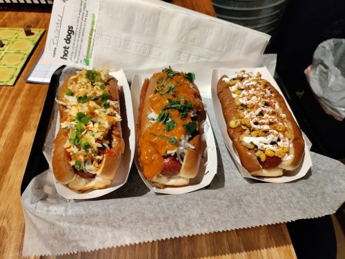 Three gourmet hot dogs on a tray, each topped with different sauces and garnishes, on a wooden table.