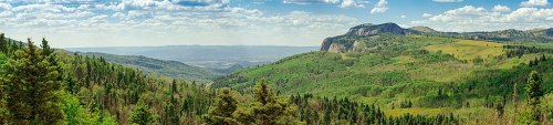 A panoramic view of lush green mountains and valleys under a blue sky with scattered clouds.