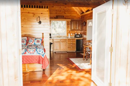 Cozy wooden cabin interior featuring a bed, kitchenette, and dining area with warm lighting.
