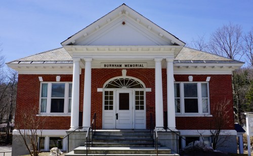 Front view of the Burnham Memorial building, featuring red brick, white columns, and a clear blue sky.