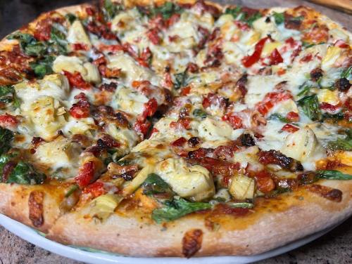 A close-up of a delicious pizza topped with spinach, artichokes, red peppers, and melted cheese on a golden crust.