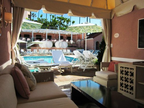 A cozy cabana overlooking a pool area with lounge chairs and umbrellas, surrounded by palm trees.