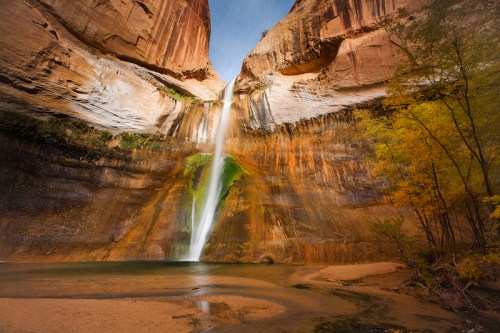 A stunning waterfall cascades down a rocky canyon, surrounded by vibrant autumn foliage and a serene pool below.