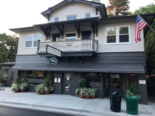A two-story building with a balcony, featuring a sign for "Calistoga Inn" and surrounded by potted plants and an American flag.