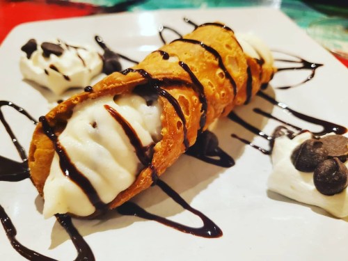 A delicious cannoli filled with creamy filling, drizzled with chocolate sauce, served with dollops of whipped cream.