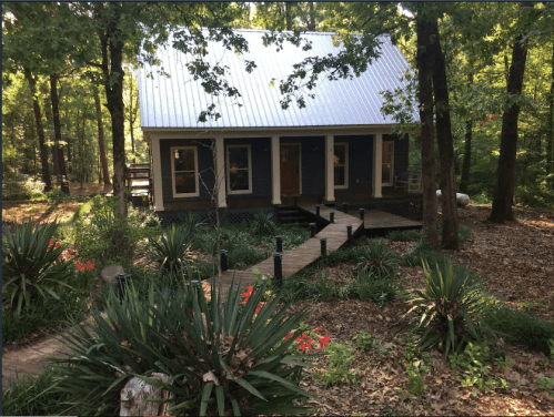 A charming house surrounded by trees and greenery, with a wooden walkway leading to the entrance.