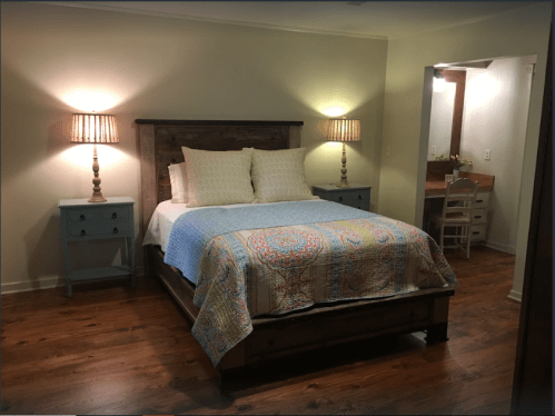 Cozy bedroom featuring a wooden bed, colorful quilt, nightstands, and warm lighting.