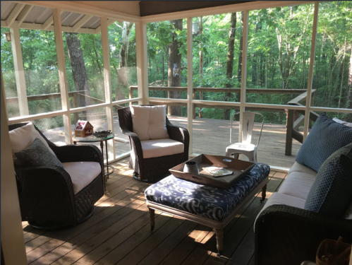 Cozy screened porch with comfortable seating, a coffee table, and a view of a wooded area outside.