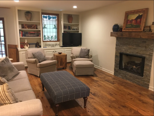 Cozy living room with a stone fireplace, comfortable seating, and bookshelves, featuring warm wood floors and decorative accents.