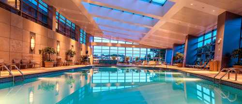 Indoor swimming pool with large windows, modern design, and soft lighting reflecting on the water's surface.