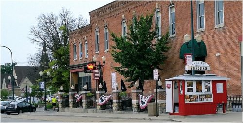 A quaint street scene featuring a brick building, outdoor seating, and a popcorn stand with patriotic decorations.