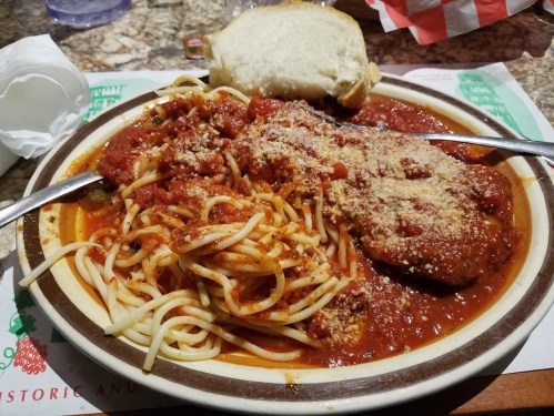 A plate of spaghetti with marinara sauce and meatballs, topped with grated cheese, served with a slice of bread.