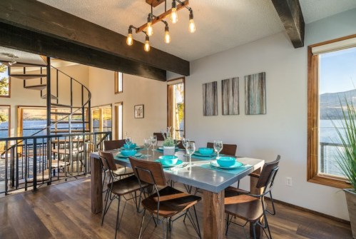 Modern dining area with a spiral staircase, large windows, and a table set with turquoise dishes overlooking a scenic view.