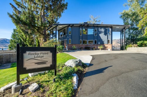Modern lodge with large windows, surrounded by greenery and mountains, featuring a sign that reads "Rocky Point Lodge."