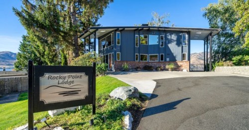 A modern lodge with large windows, surrounded by greenery, and a sign reading "Rocky Point Lodge" in front.