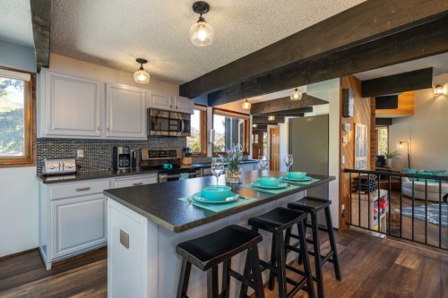 Modern kitchen with a dark countertop, bar stools, and stylish lighting, featuring gray cabinets and a cozy dining setup.