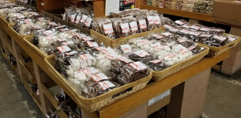 A display of various packaged snacks in baskets on a wooden table at a market.