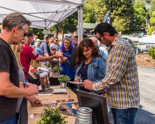 A crowd gathers at an outdoor event, engaging at tables with displays and products under a tent.